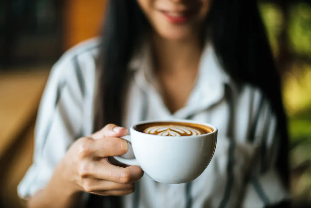 Mulher tomando café durante o trabalho, representando o impacto do excesso na produtividade.