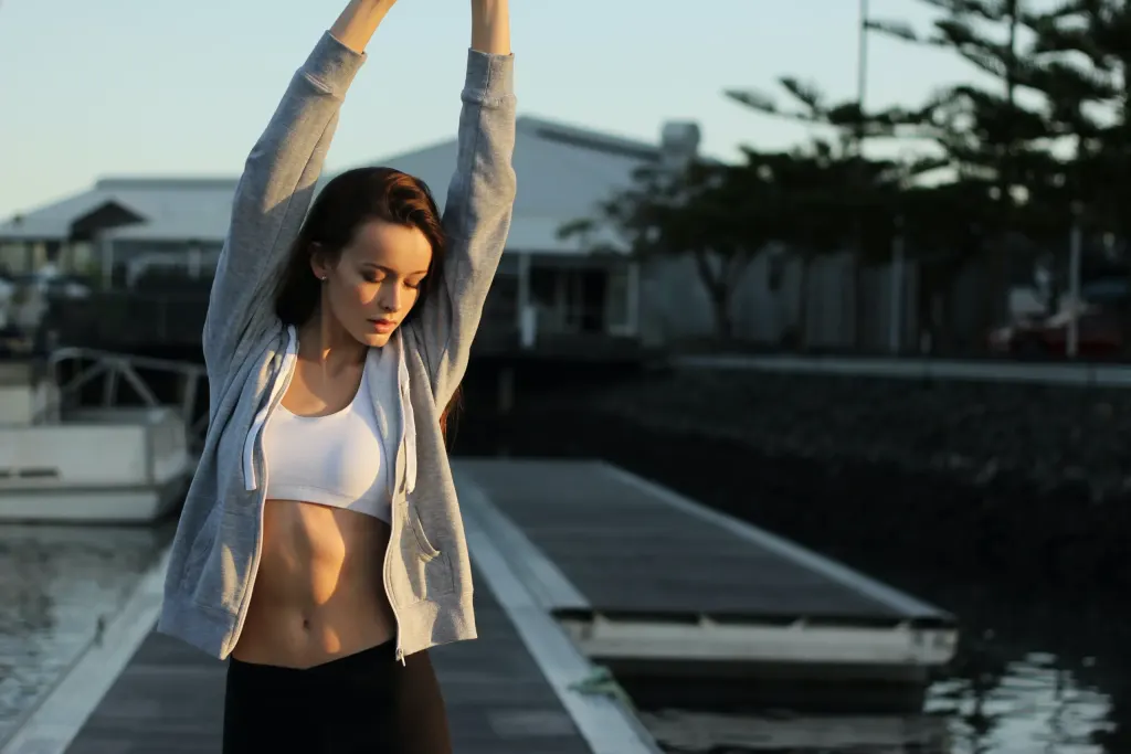 Mulher faz exercícios de alongamento na rua. Imagem mostra a prática da atividade física, um dos pilares de como cuidar da saúde mental e emocional.