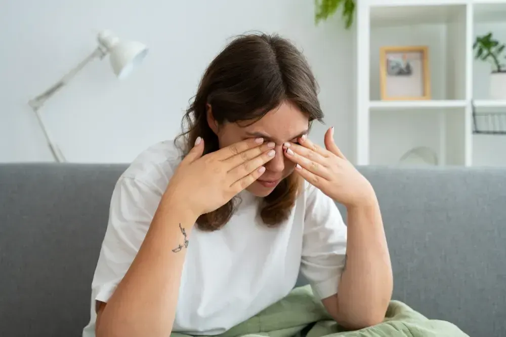 Mulher leva às mãos aos olhos coçando pois está com cojuntivite alérgica.,