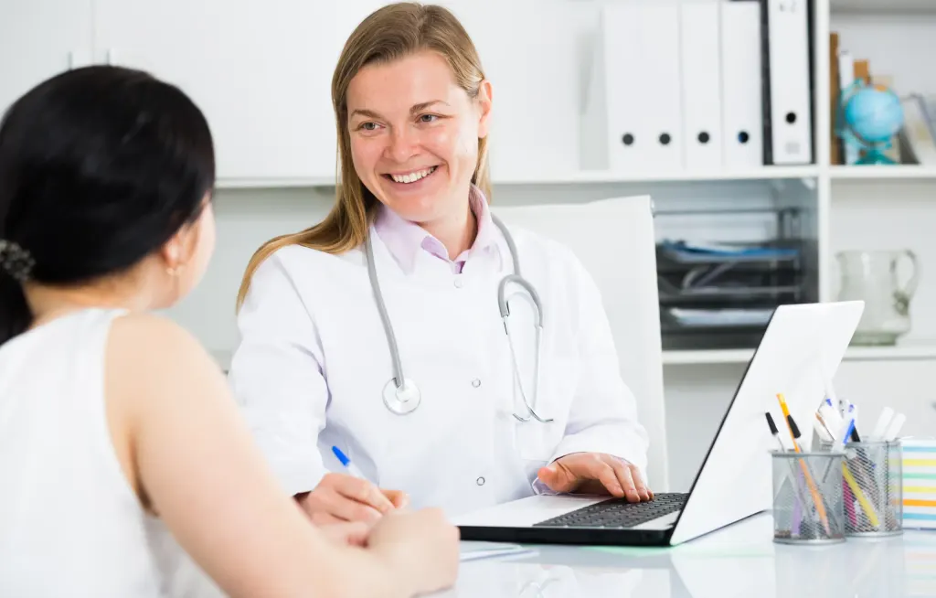 Paciente está em uma sala realizando consulta médica com um médico de jaleco. A imagem representa o diagnóstico de dor nas mamas.