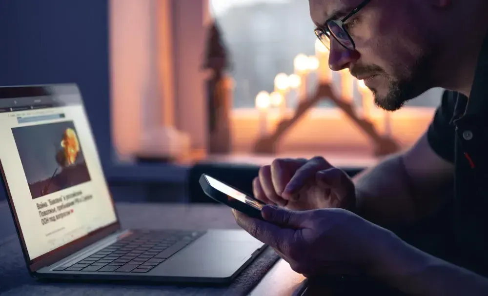 Homem está com excesso de telas usando notebbok e celular ao mesmo tempo.