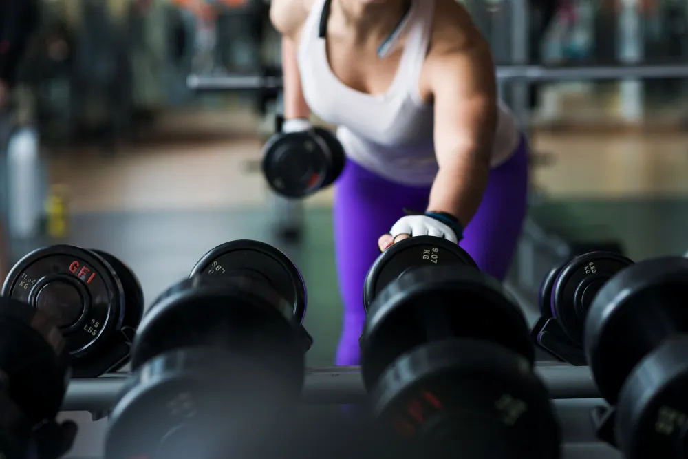 Mulher está em uma academia escolhendo pesos para fazer o fortalecimento muscular.