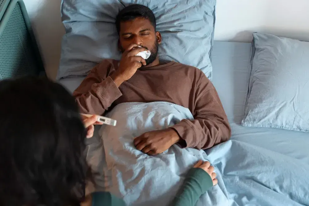 Homem está com febre deitando na cama e apresenta sintomas de hepatite viral.