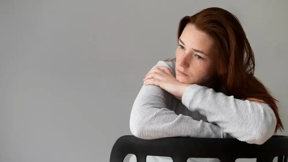 Mulher está no consultório e pergunta "O que é anedonia?". Na imagem ela aparenta estar desanimada.