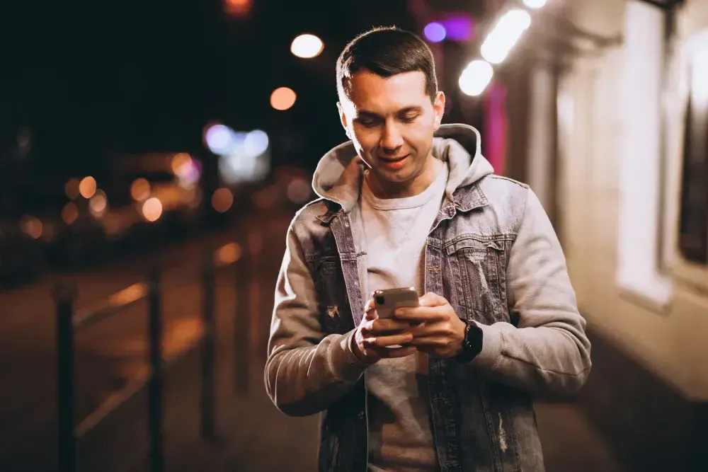 Homem está na rua e lê no celular o que é nomofobia.